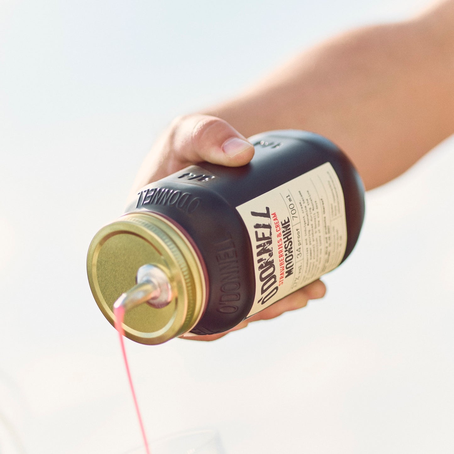 Eine Hand, die aus einem Glas Strawberry Cream Likör einschenkt