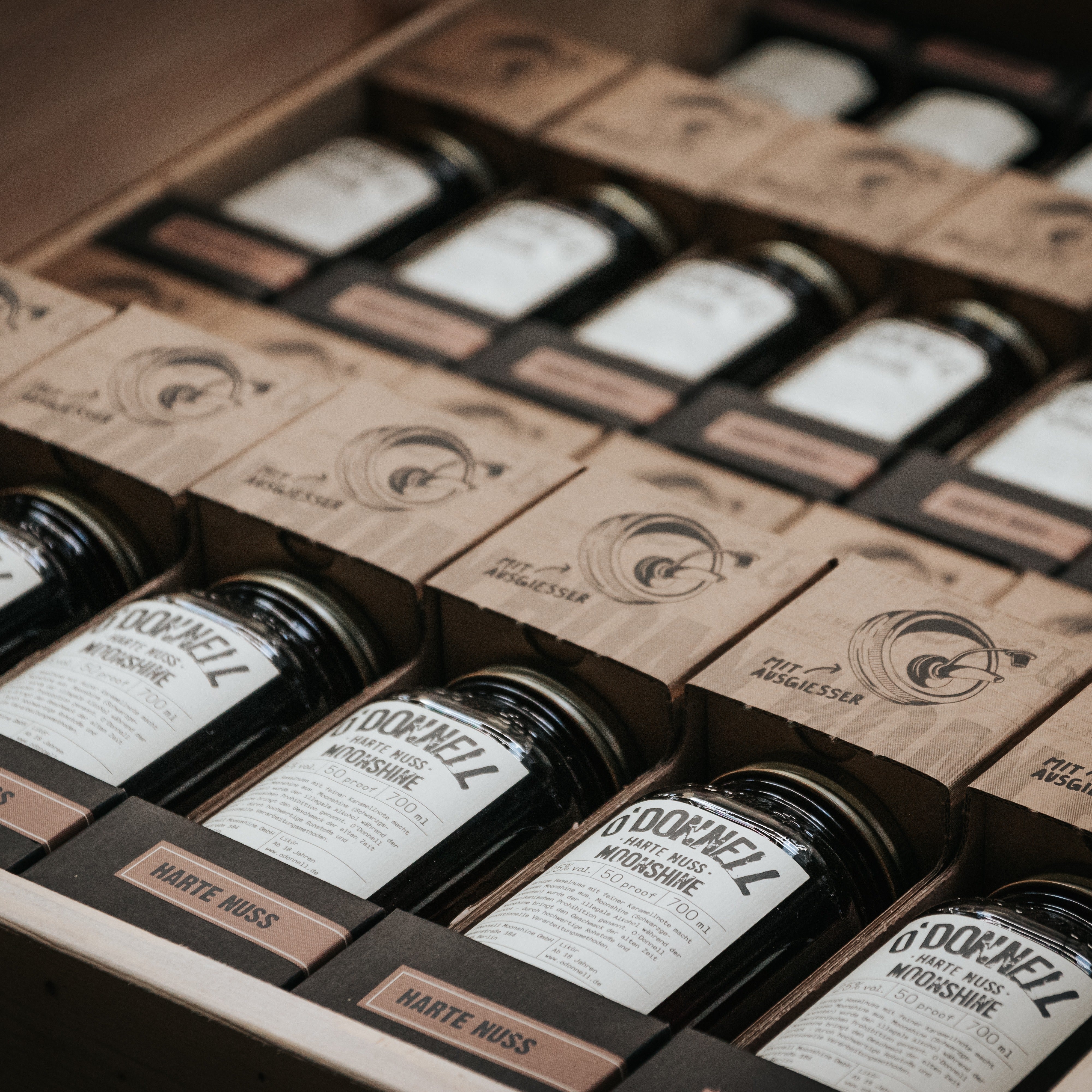 Mehrere Verkaufsverpackungen von O'Donnell Moonshine der Sorte „Harte Nuss“ in Mason Jars, aufgereiht in einer Kiste mit dem Hinweis „Mit Ausgießer“.
