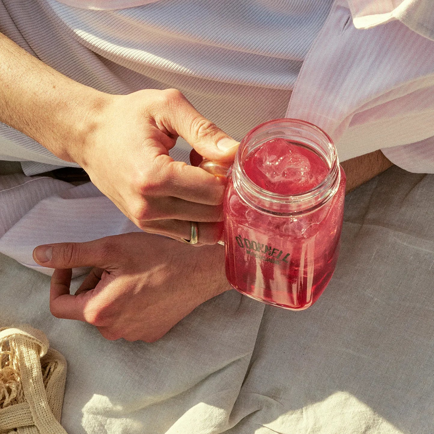 Person hält O'Donnell Moonshine Henkelglas mit rotem Cocktail und Eis in beiden Händen – Nahaufnahme, Outdoor-Lifestyle
