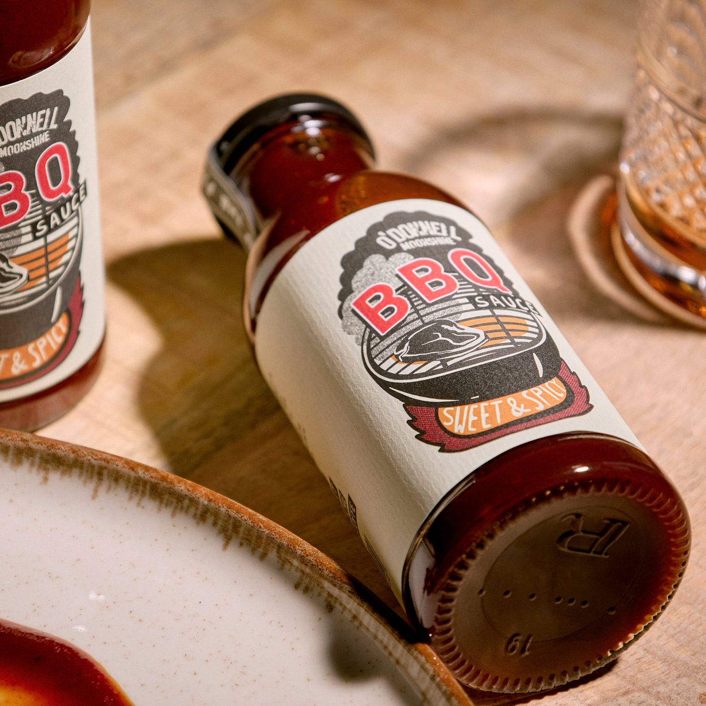 O'Donnell Moonshine BBQ Sauce Sweet & Spicy – zwei Flaschen auf warmem Untergrund, angeschrägte Vogelperspektive mit dunkler Studioatmosphäre