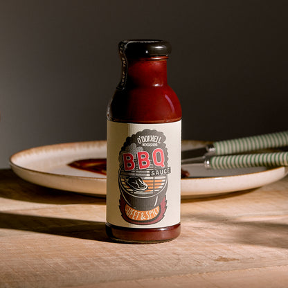 O'Donnell Moonshine BBQ Sauce Sweet & Spicy – Flasche auf Holzunterlage mit Tellern im Hintergrund, dunkle Studioatmosphäre