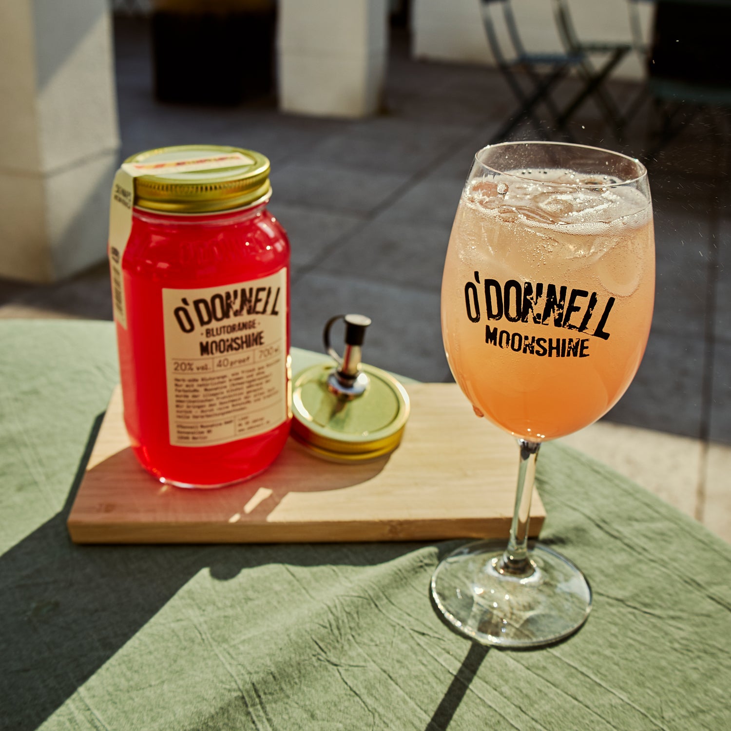 Ein volles Spritzglas, ein mit Blutorange gefärbtes Getränk und ein Stövchen auf einem Tisch mit Fokus auf den Spritzglas