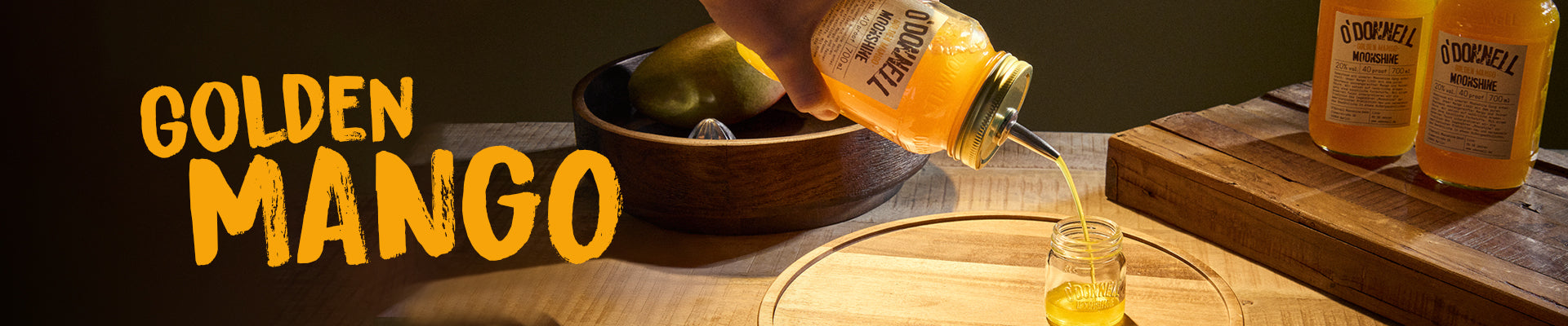 Goldenes Mango-Banner. Eine Hand hält ein Glas mit Mango-Likör und gießt ihn in ein Schnapsglas.