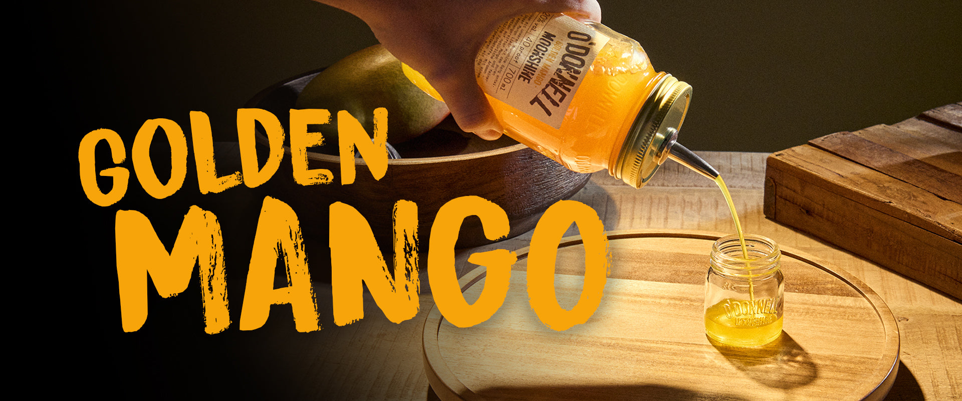Goldenes Mango-Banner. Eine Hand hält ein Glas mit Mango-Likör und gießt ihn in ein Schnapsglas.