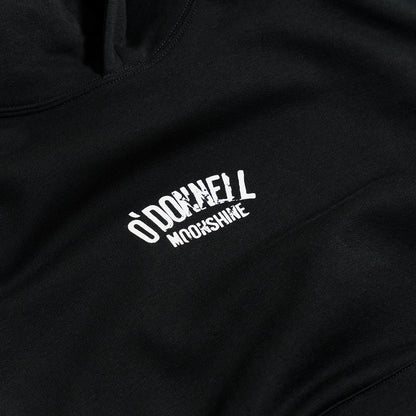 Quadratische Detailaufnahme für O'Donnell Moonshine: Ein weißer Logo-Print der Marke im Vintage-Stil prallt auf der Brust eines schwarzen Hoodies ab.