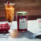 Very Vodka Cherries in einem Einmachglas vor einem hölzernen Hintergrund, neben einem eisgekühlten Cola-Getränk und frischen Kirschen
