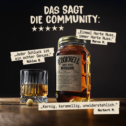 Ein großes Likörglas der Sorte „Harte Nuss“, ein gefülltes Tumbler-Glas mit Eiswürfeln und lose Haselnüsse stehen auf rustikalem Holz.