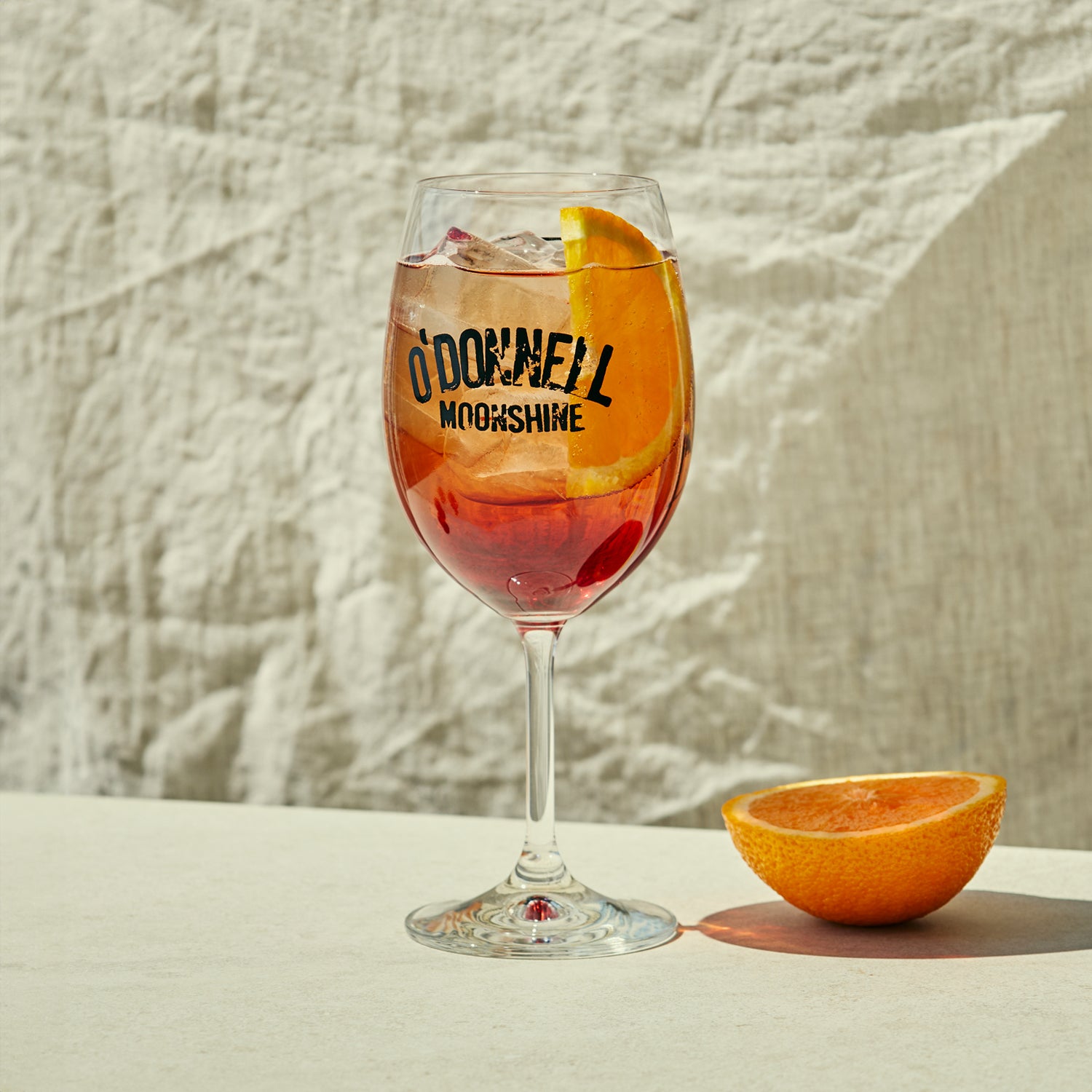 Ein volles Sprtizglas mit einer halben Orange daneben
