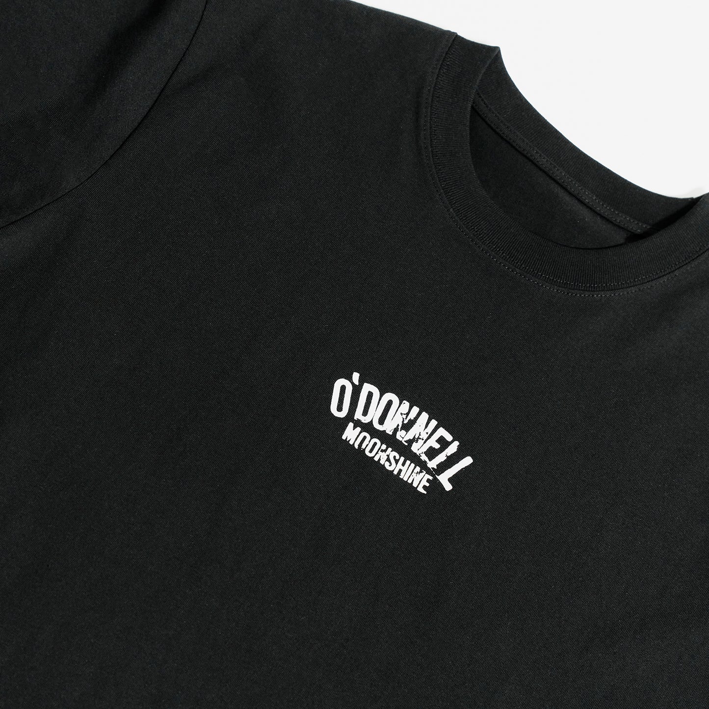 Quadratische Detailansicht für O'Donnell Moonshine: Ein kleiner, weißer Marken-Logoprint im Vintage-Look befindet sich auf der Brust eines schwarzen T-Shirts.