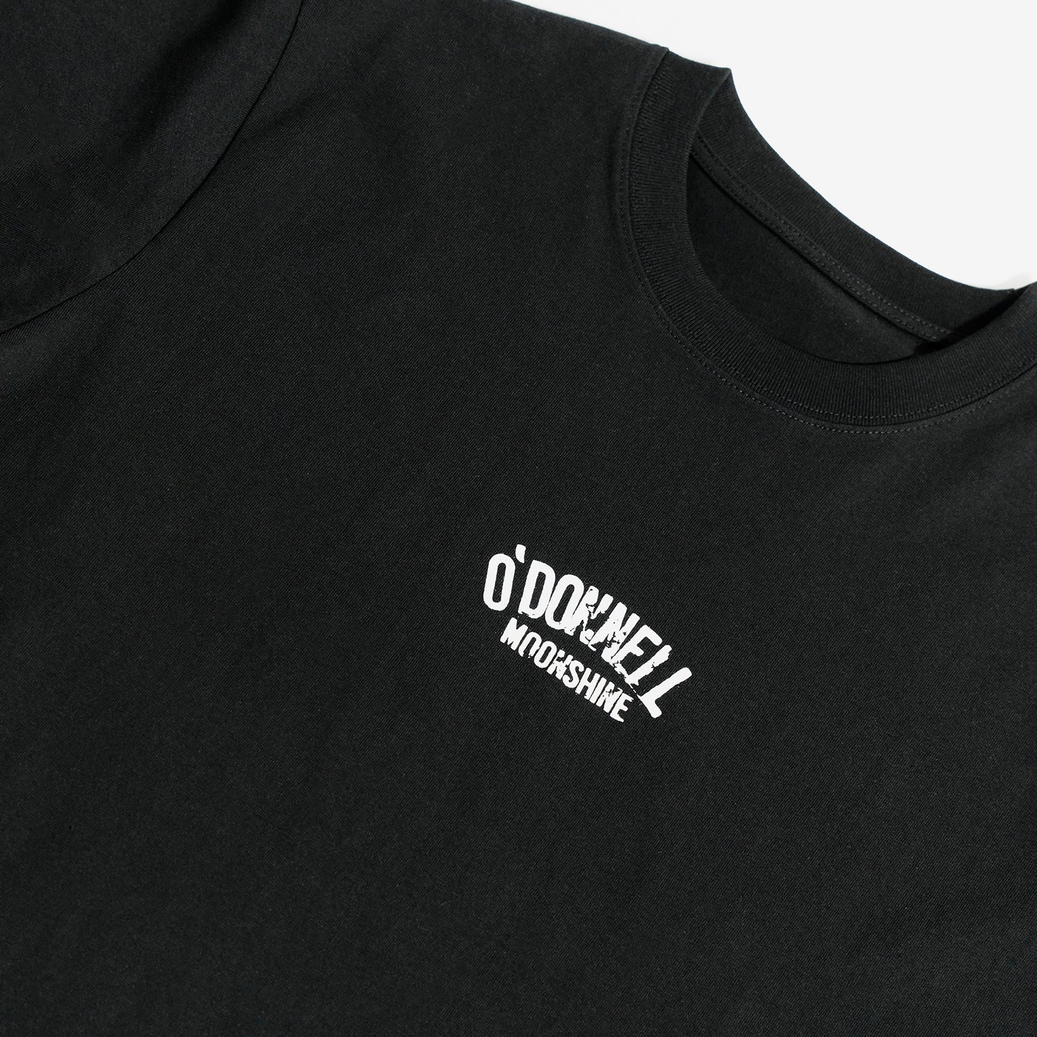 Quadratische Detailansicht für O'Donnell Moonshine: Ein kleiner, weißer Marken-Logoprint im Vintage-Look befindet sich auf der Brust eines schwarzen T-Shirts.