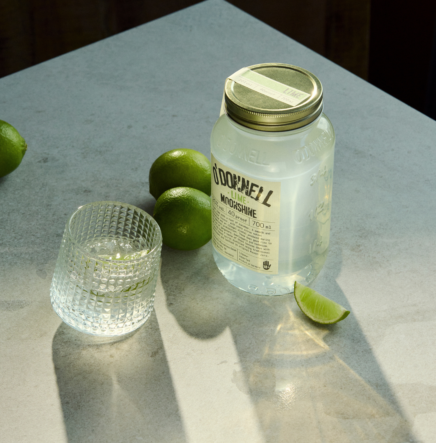 O'Donnell Moonshine Limette 700ml auf Marmoroberfläche – Lifestyle-Foto mit frischen Limetten und Cocktailglas, stimmungsvolle Beleuchtung