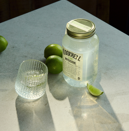 O'Donnell Moonshine Limette 700ml auf Marmoroberfläche – Lifestyle-Foto mit frischen Limetten und Cocktailglas, stimmungsvolle Beleuchtung