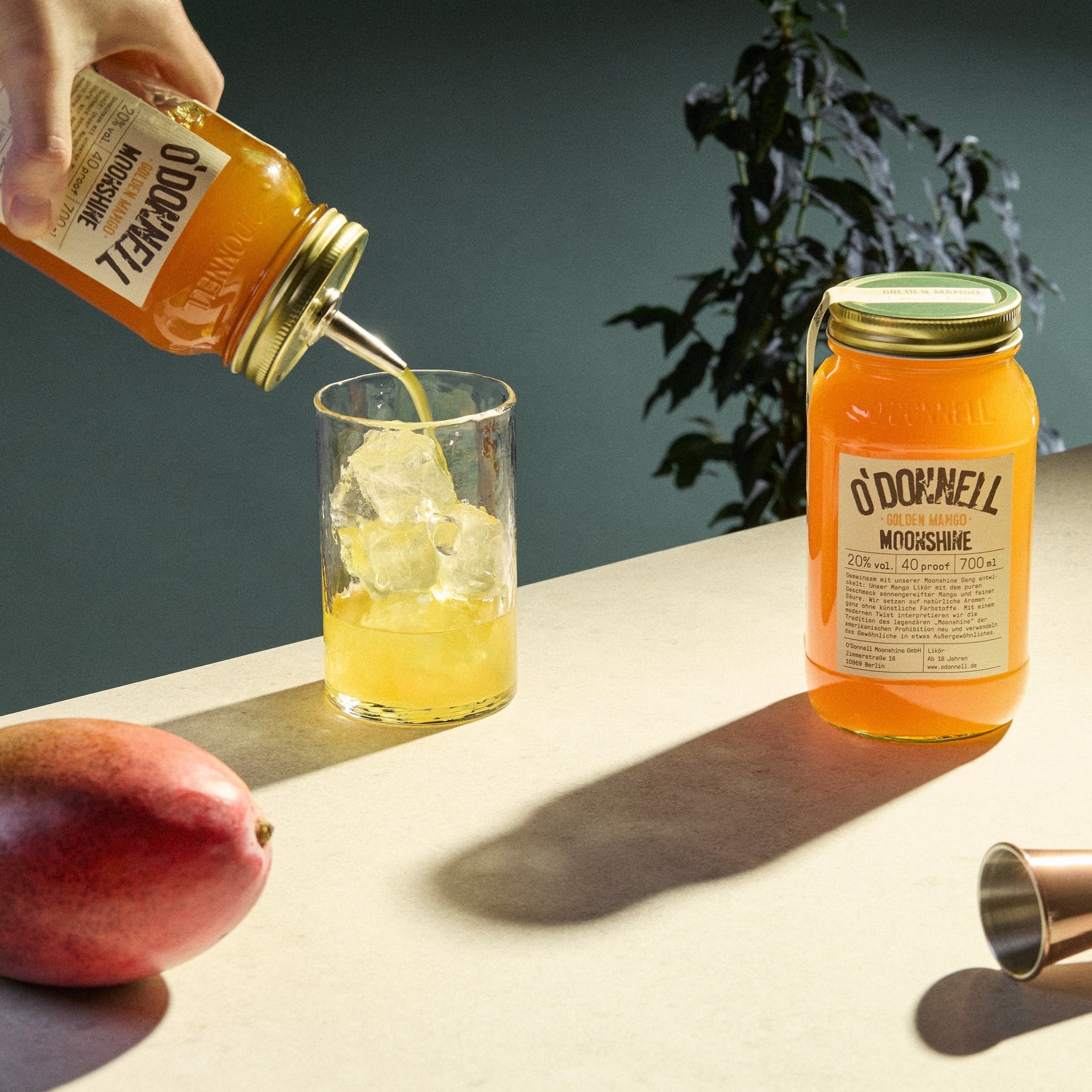 Der O'Donnell Moonshine Glden mango Likör präsentiert mit einem Cocktail und einer frischen Mango.