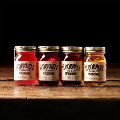Vier kleine O'Donnell Moonshine Likörflaschen (50ml) der Sommersorten auf rustikalem Holz vor schwarzem Hintergrund.