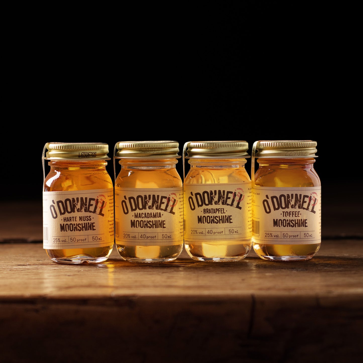 Vier kleine O'Donnell Moonshine Likörflaschen (50ml) der Wintersorten auf rustikalem Holz vor schwarzem Hintergrund.