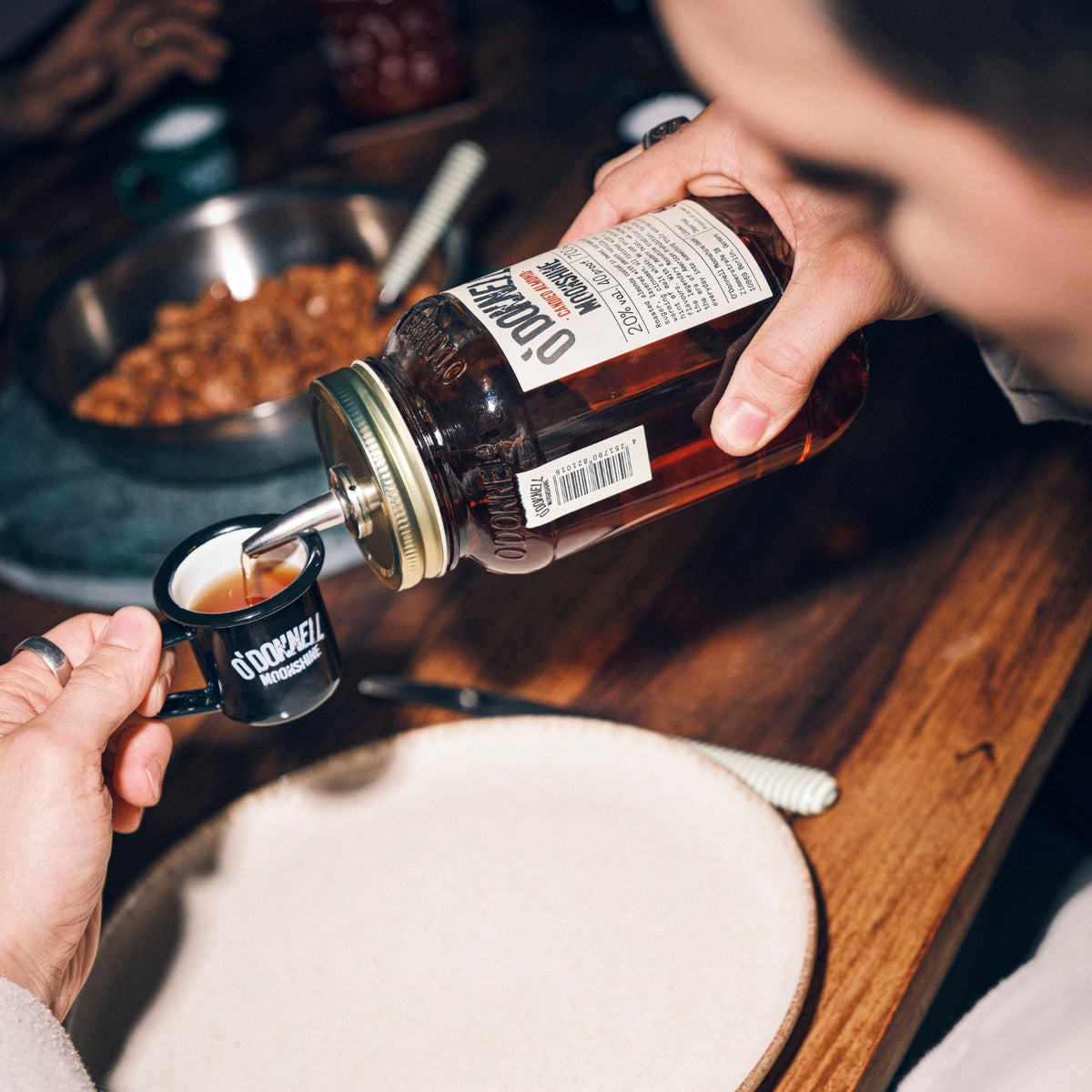 O'Donnell Moonshine Likör der Sorte Candied Almond wird mit einem Ausgießer in eine kleine, schwarze Tasse eingeschenkt.