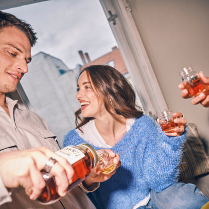 Zwei Personen lachen am Fenster, während O'Donnell Moonshine Likör in kleine Gläser für einen Toast eingeschenkt wird.