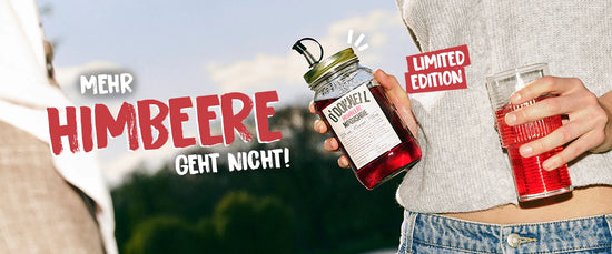 Eine Frau erhält O'Donnell Moonshine Himbeere Flasche und Cocktailglas im Freien vor blauem Himmel