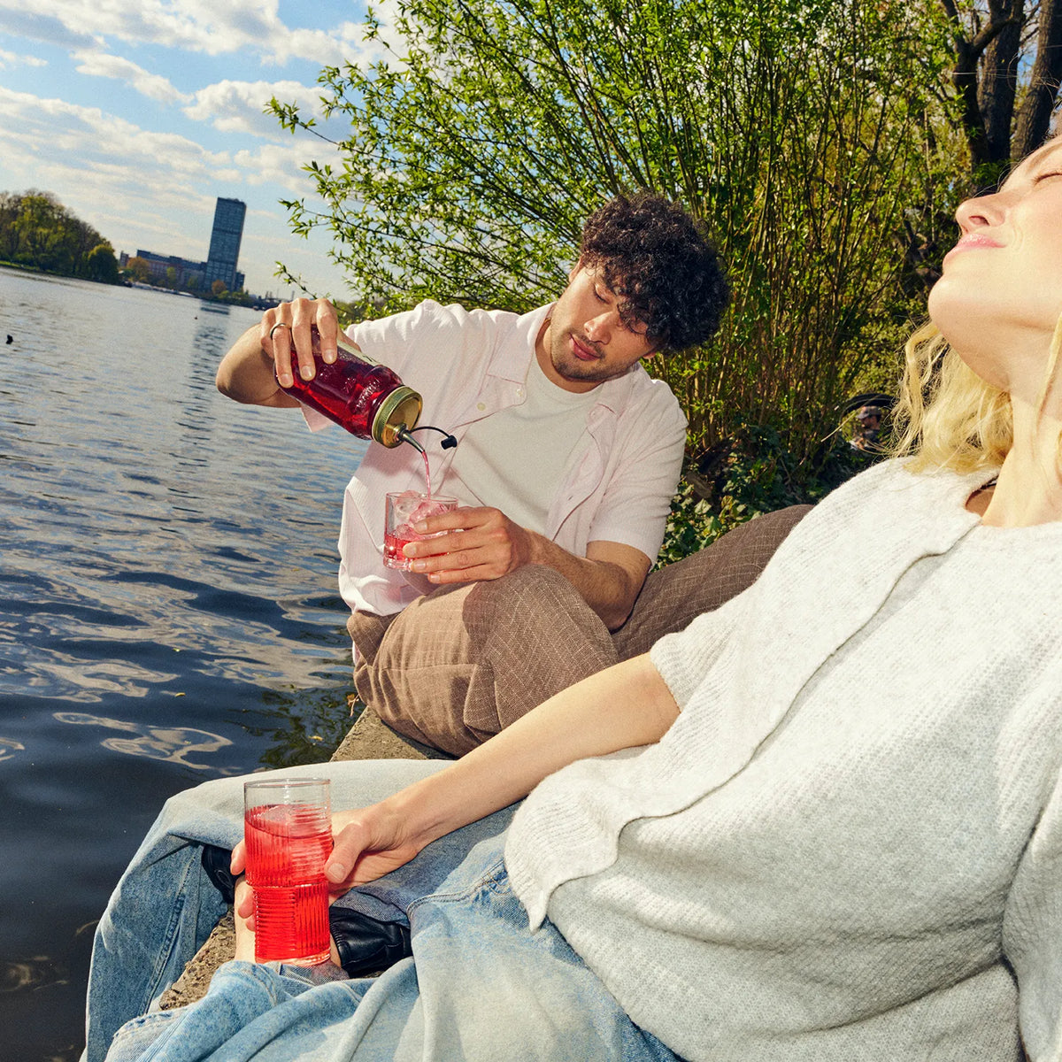 Mann schenkt einer Frau O'Donnell Moonshine Himbeere in ein Cocktailglas ein – Sommer-Lifestyle am See, im Freien