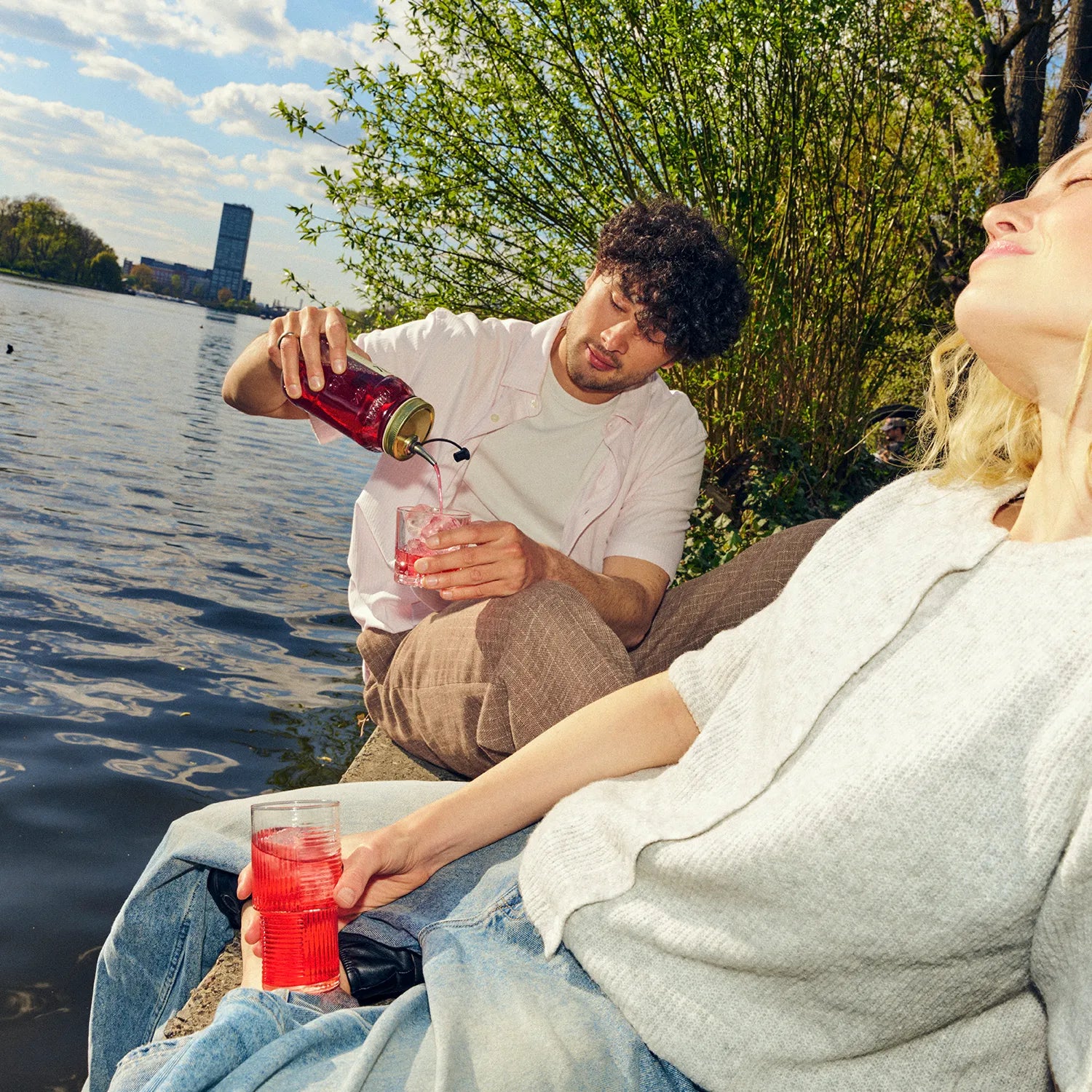 Mann schenkt einer Frau O'Donnell Moonshine Himbeere in ein Cocktailglas ein – Sommer-Lifestyle am See, im Freien
