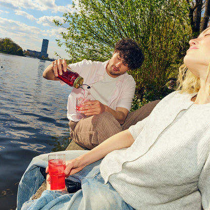Mann schenkt einer Frau O'Donnell Moonshine Himbeere in ein Cocktailglas ein – Sommer-Lifestyle am See, im Freien