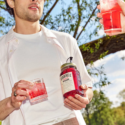 Mann hält O'Donnell Moonshine Himbeere Flasche und Cocktailglas im Freien unter Bäumen