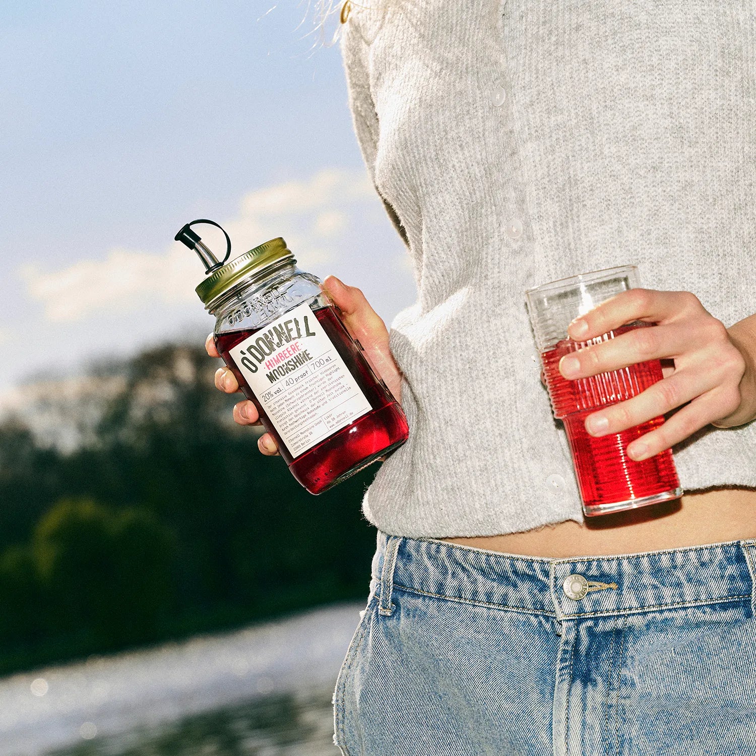 Person hält O'Donnell Moonshine Himbeere Flasche und Cocktailglas im Freien