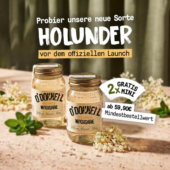 Zwei kleine O'Donnell Moonshine Holunder-Minigläser stehen inmitten von weißen Holunderblüten im warmen Sonnenlicht.