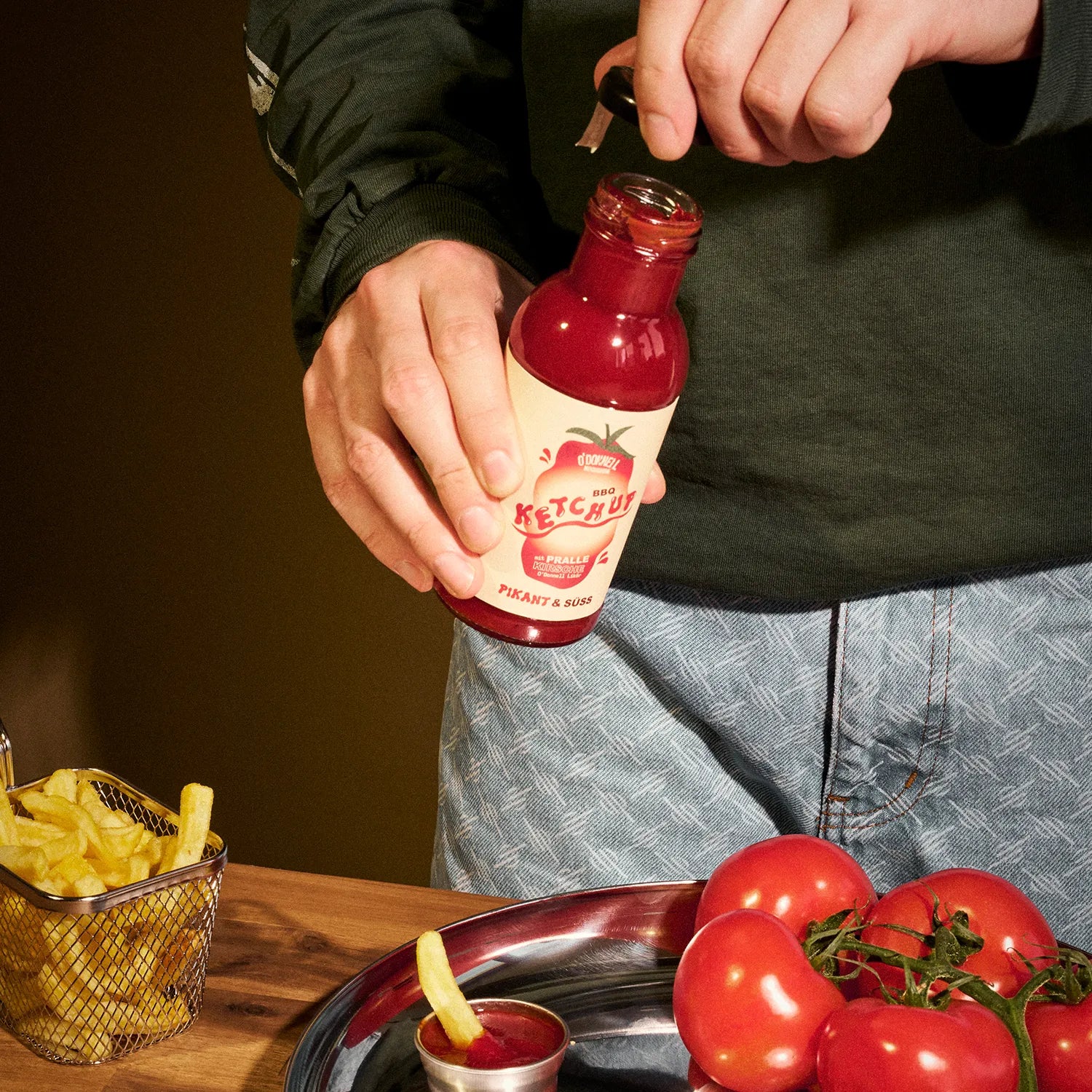 O'Donnell Moonshine BBQ Ketchup Pikant & Süss – Person öffnet die Flasche über einem Tisch mit Pommes-Korb, Tomaten und Dipschale
