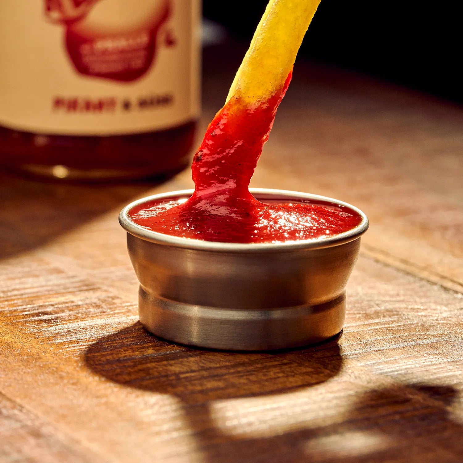 O'Donnell Moonshine BBQ Ketchup Pikant & Süss – Pommes-Frites wird in eine Metallschale mit Ketchup getaucht, Flasche im Hintergrund, dunkle Lichtstimmung