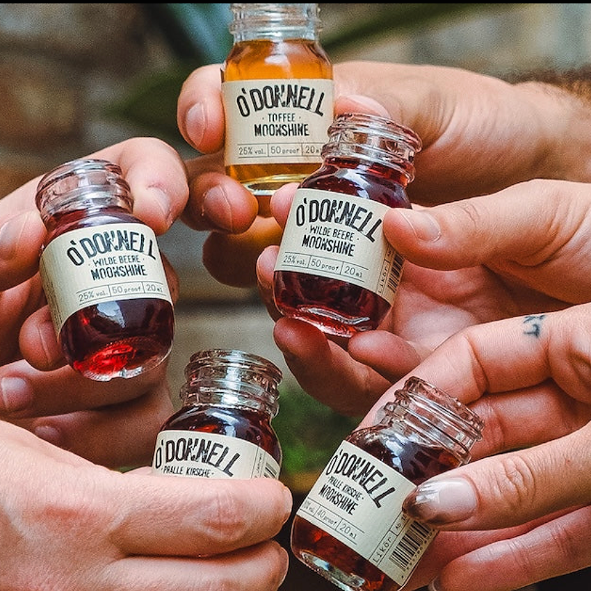 Eine Gruppe hält fünf O'Donnell Moonshine Minis 50ml zum Anstoßen in die Mitte