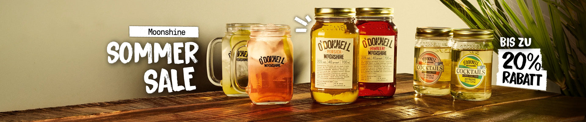 Extrem breitformatiges Desktop-Homepage-Banner für O'Donnell Moonshine, inszeniert auf einer rustikalen Holzoberfläche im warmen Streulicht. Gezeigt wird ein Produkt-Ensemble aus zwei servierten Cocktails in Gläsern mit Henkel, den großen Likörsorten „Pfirsich“ und „Himbeere“ sowie zwei kleineren „Cocktails“-Gläsern ganz rechts. 