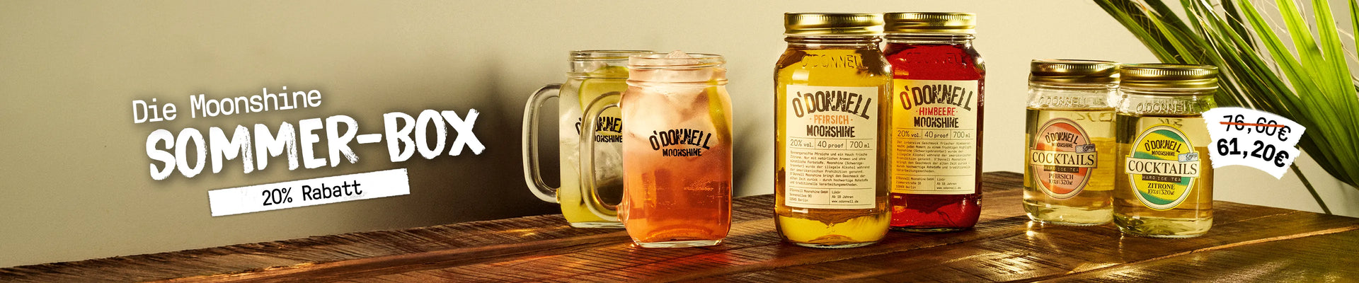 Desktop-Banner für die O'Donnell Moonshine Sommer-Box auf einem Holztisch. Zu sehen sind zwei gefüllte Cocktail-Gläser, zwei Moonshine-Flaschen (Pfirsich und Himbeere) sowie zwei Cocktail-Mixer vor hellem Hintergrund mit einer Palme. Text: „Die Moonshine Sommer-Box – 20% Rabatt“.