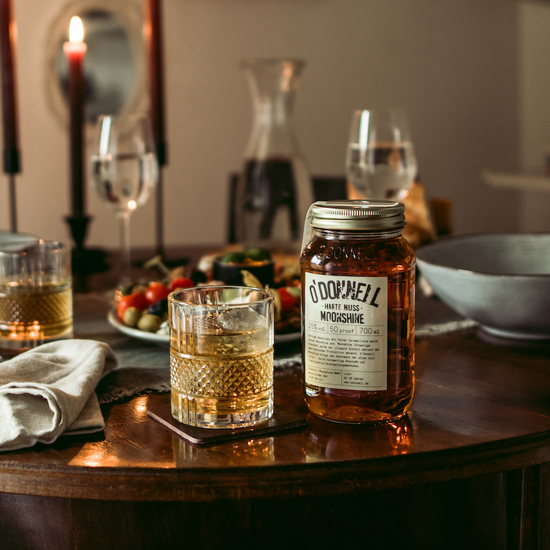 Die O'Donnell Moonshine Harte Nuss neben einem Nutty Toddy Cocktail auf einem reich gedecktem Esstisch. 
